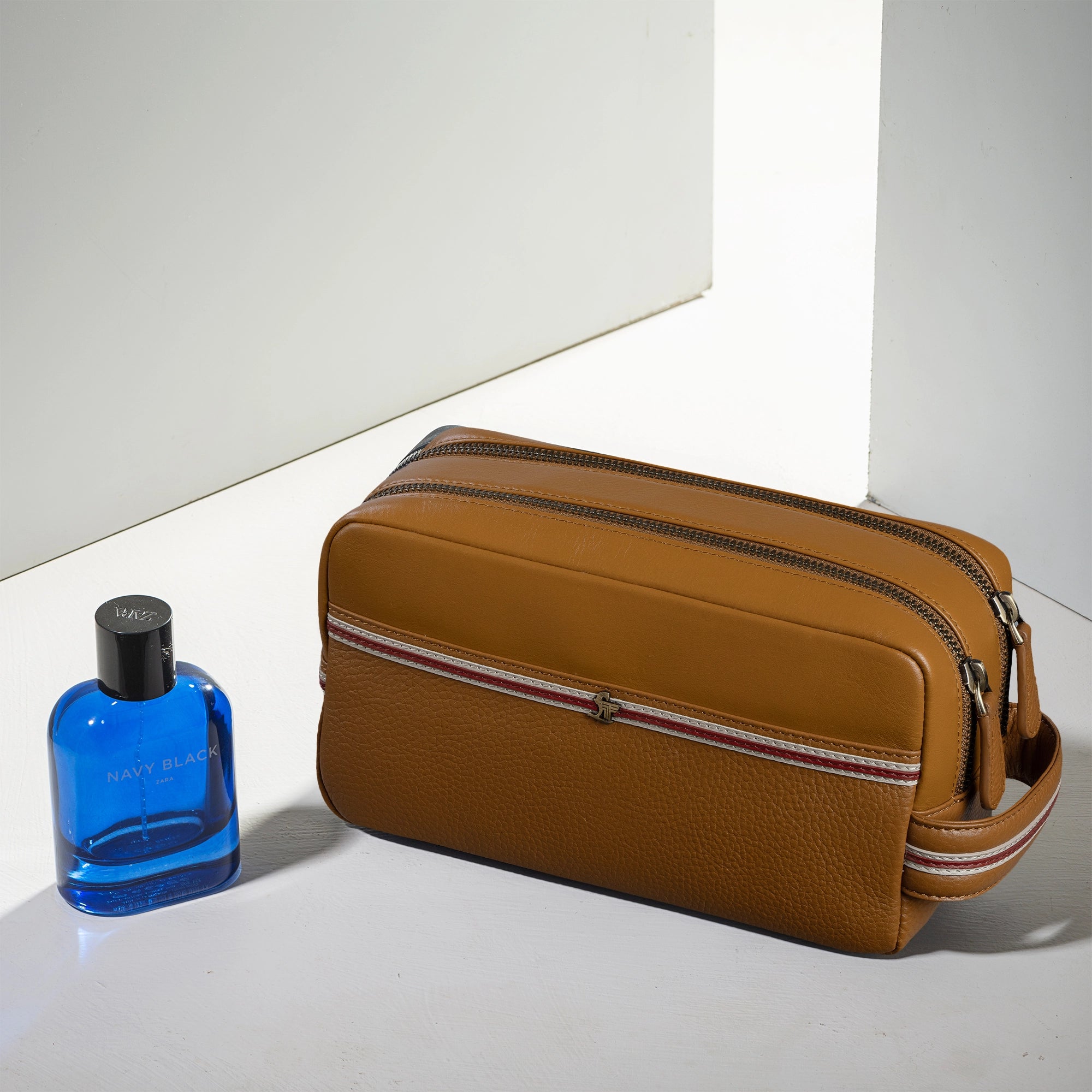 Brown leather toiletry bag with a blue bottle on a white surface