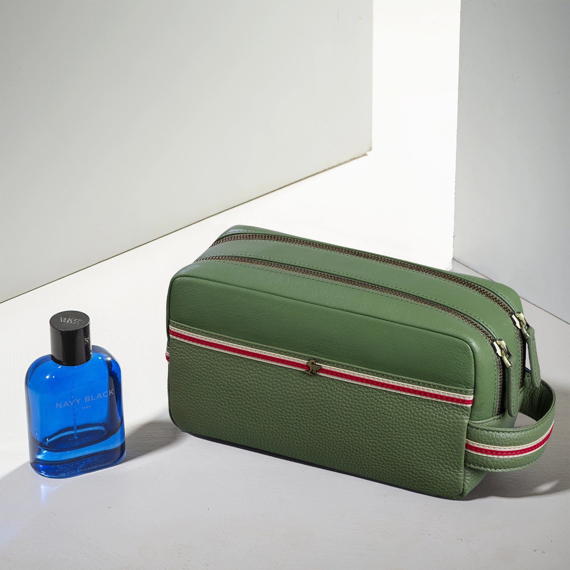 Green toiletry bag with red and white stripe next to a blue bottle on a light background
