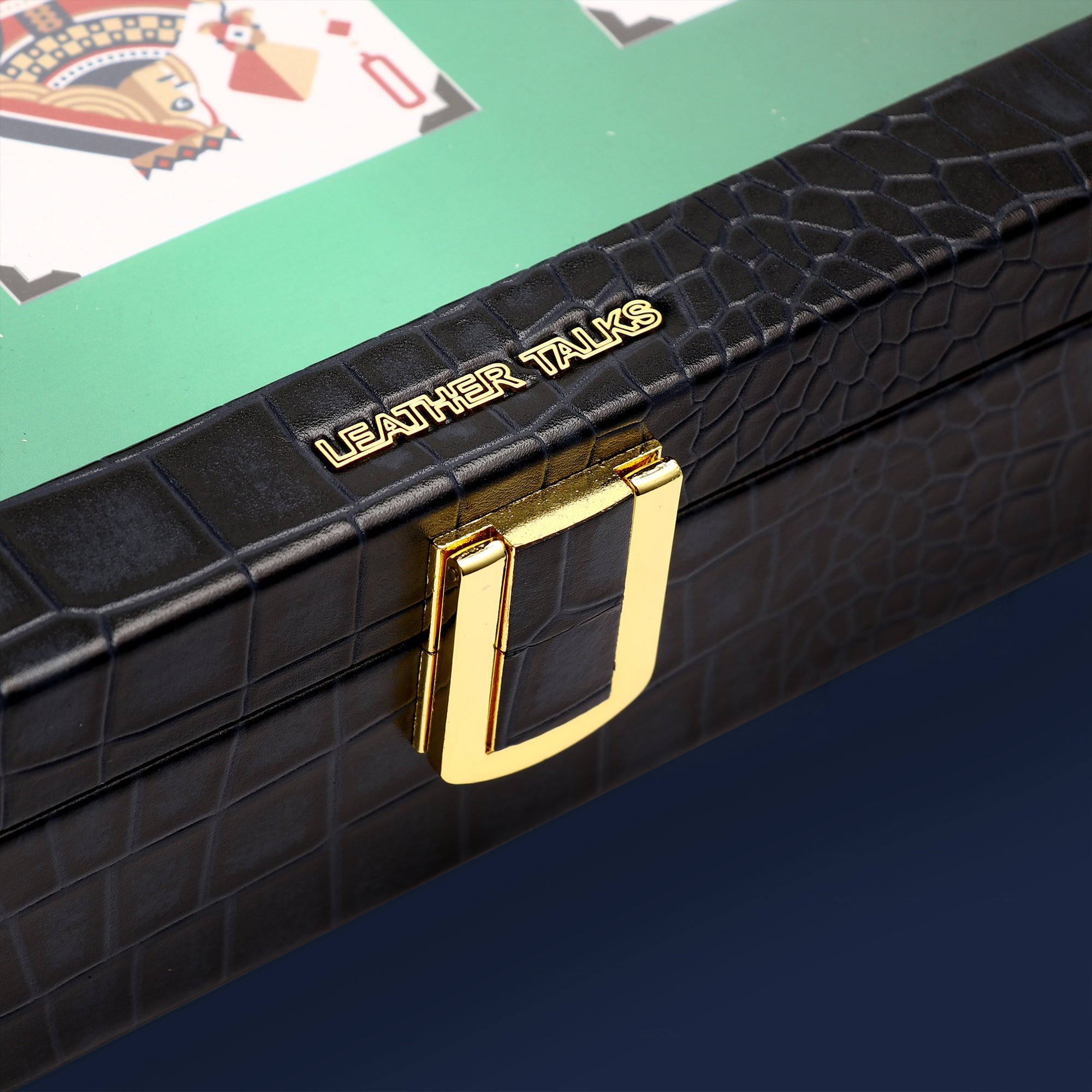 Blue crocodile-patterned leather case with gold handle and 'LEATHER TALKS' branding, on a green surface.