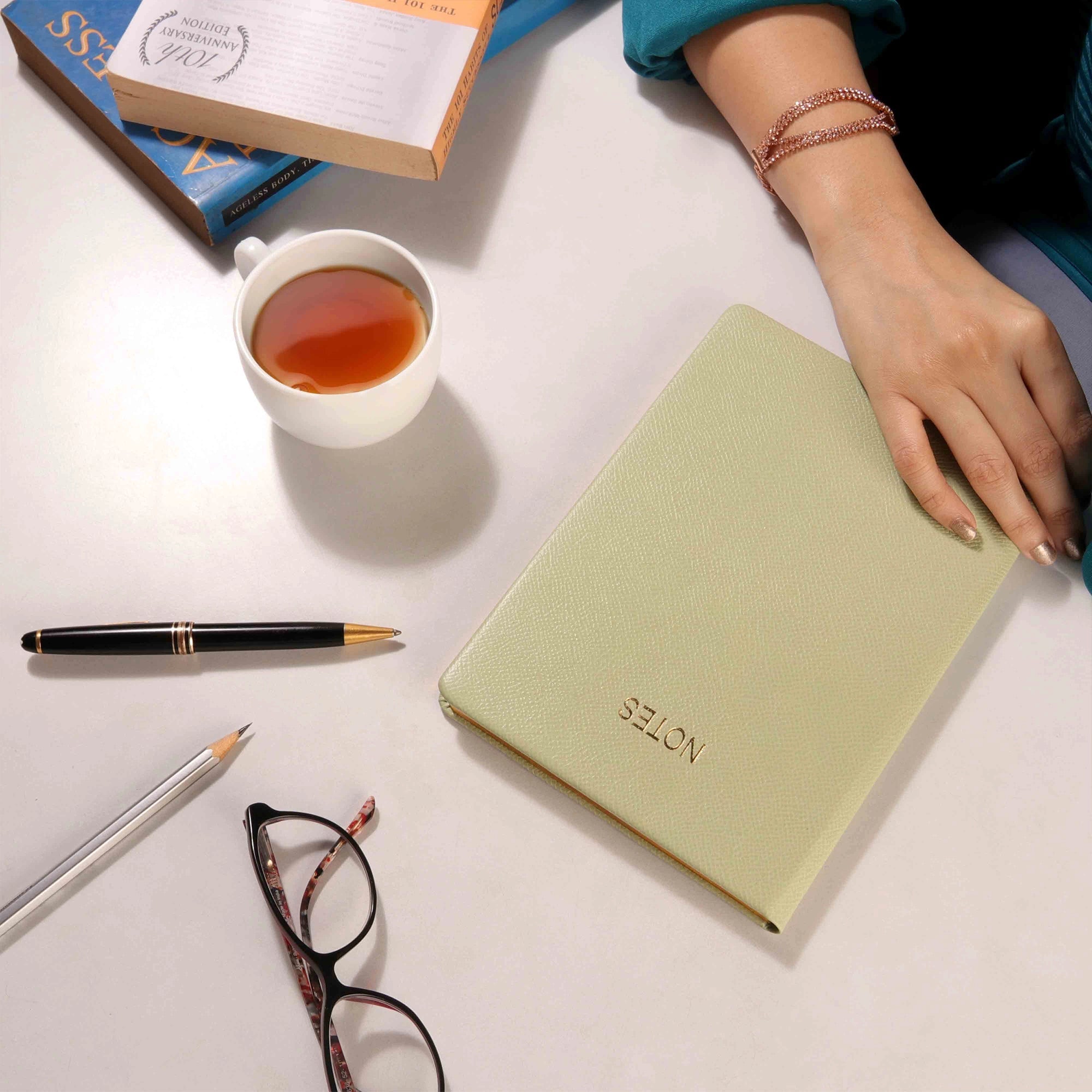Closed leather notebook on desk with tea cup and stationery