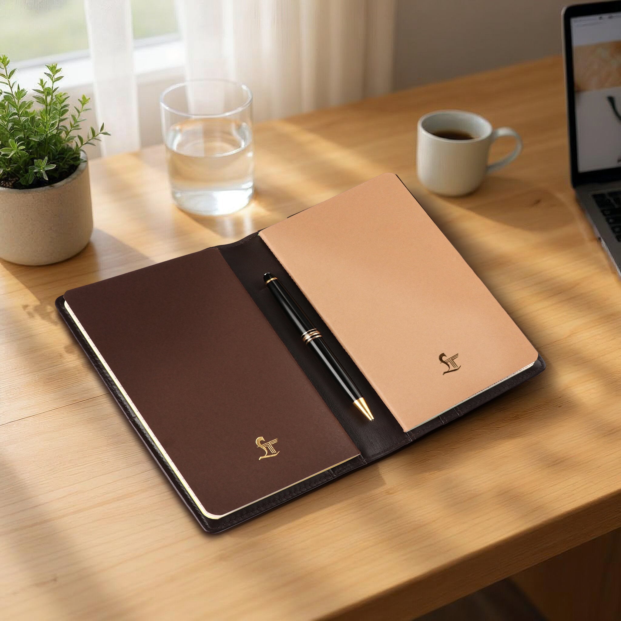 Open leather notebook with pen on a wooden desk with a cup of coffee and plant in the background.