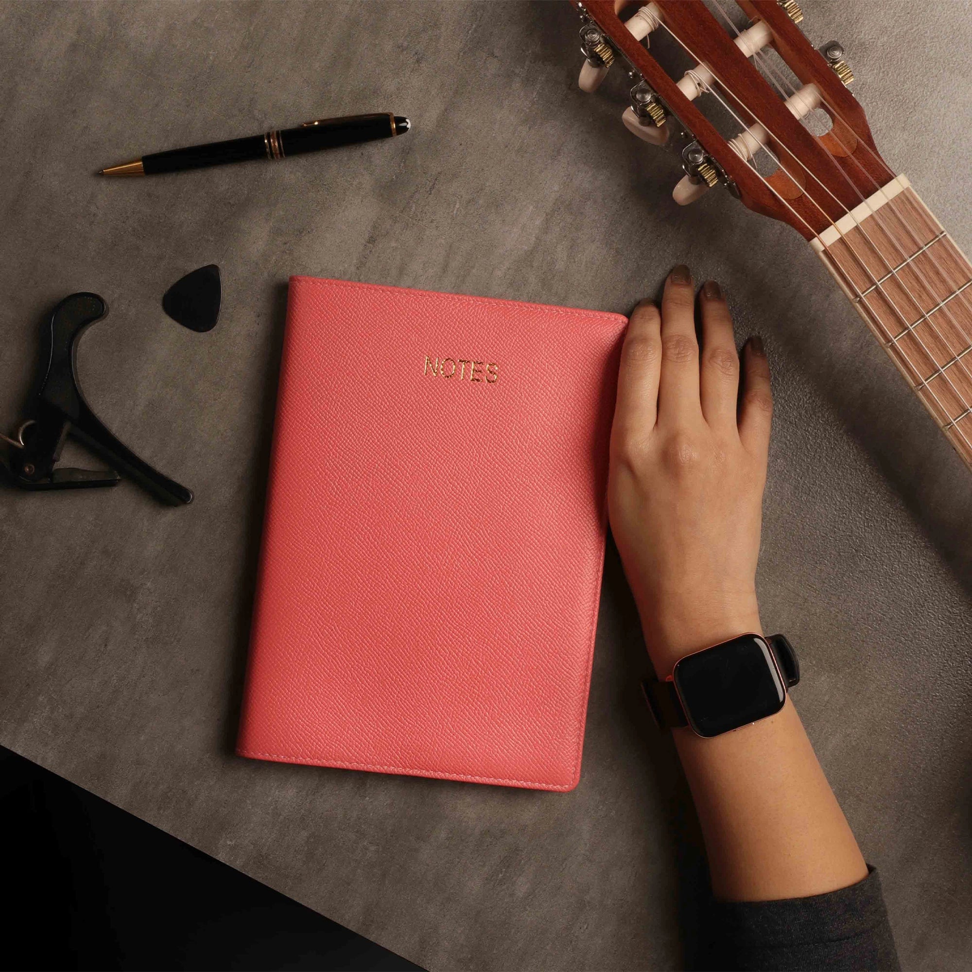 Closed leather notebook on desk with tea cup and stationery
