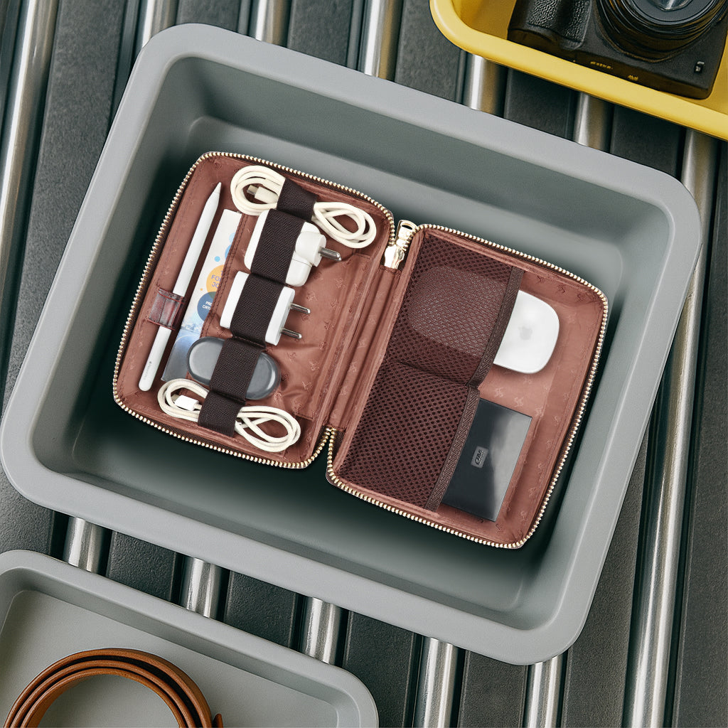 Brown travel accessory case with electronic items on a metal surface